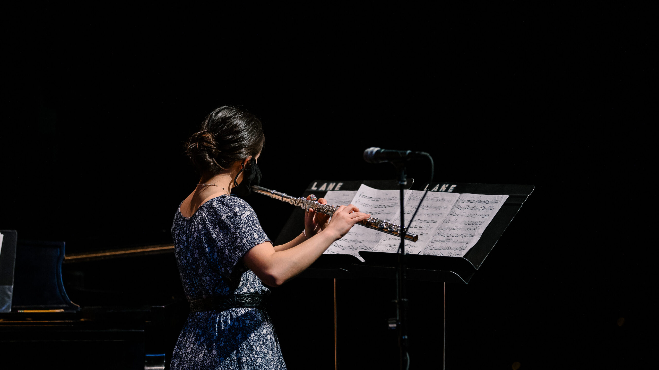 Lily Wong stands on a stage playing the flute. 