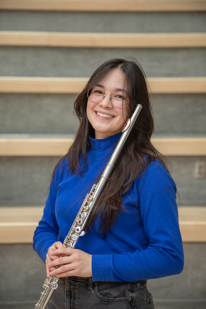 Headshot of Lily Wong wearing a blue turtleneck and holding a flute.